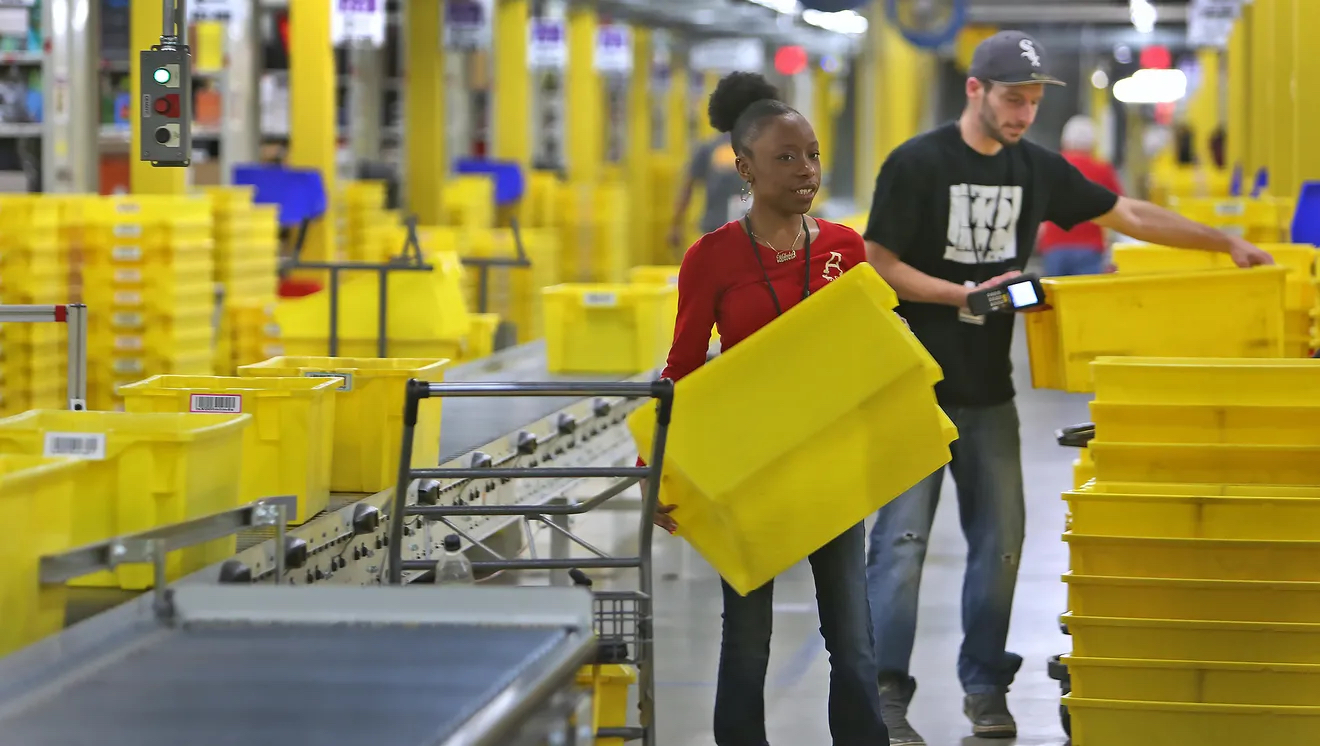 A woman and a man stack yellow totes in a warehouse. 