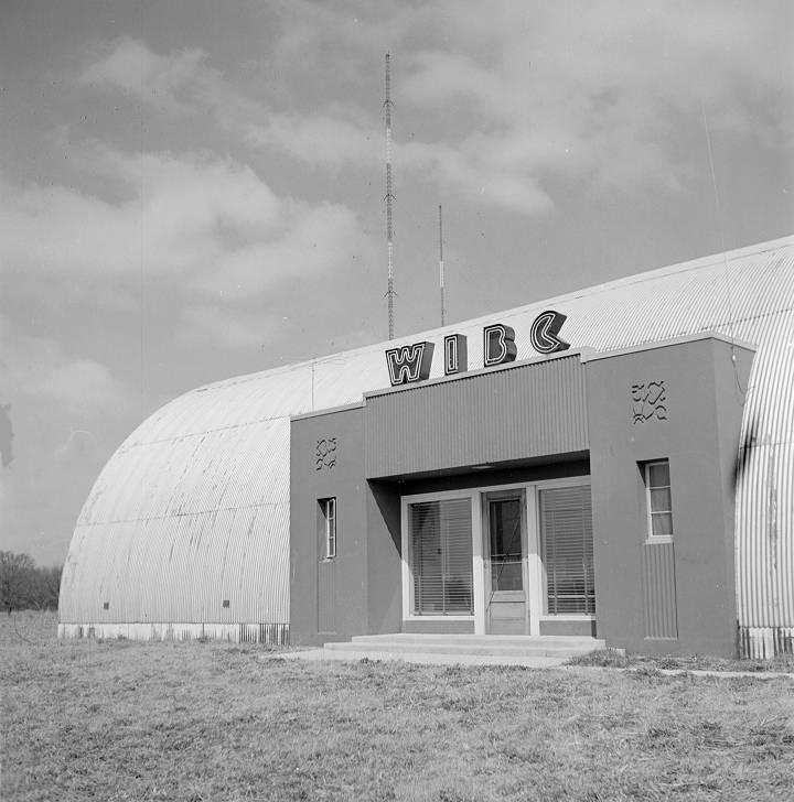 Exterior view of a radio station building with rounded edges. The letters W I B C are affixed to the top of the entrance. 