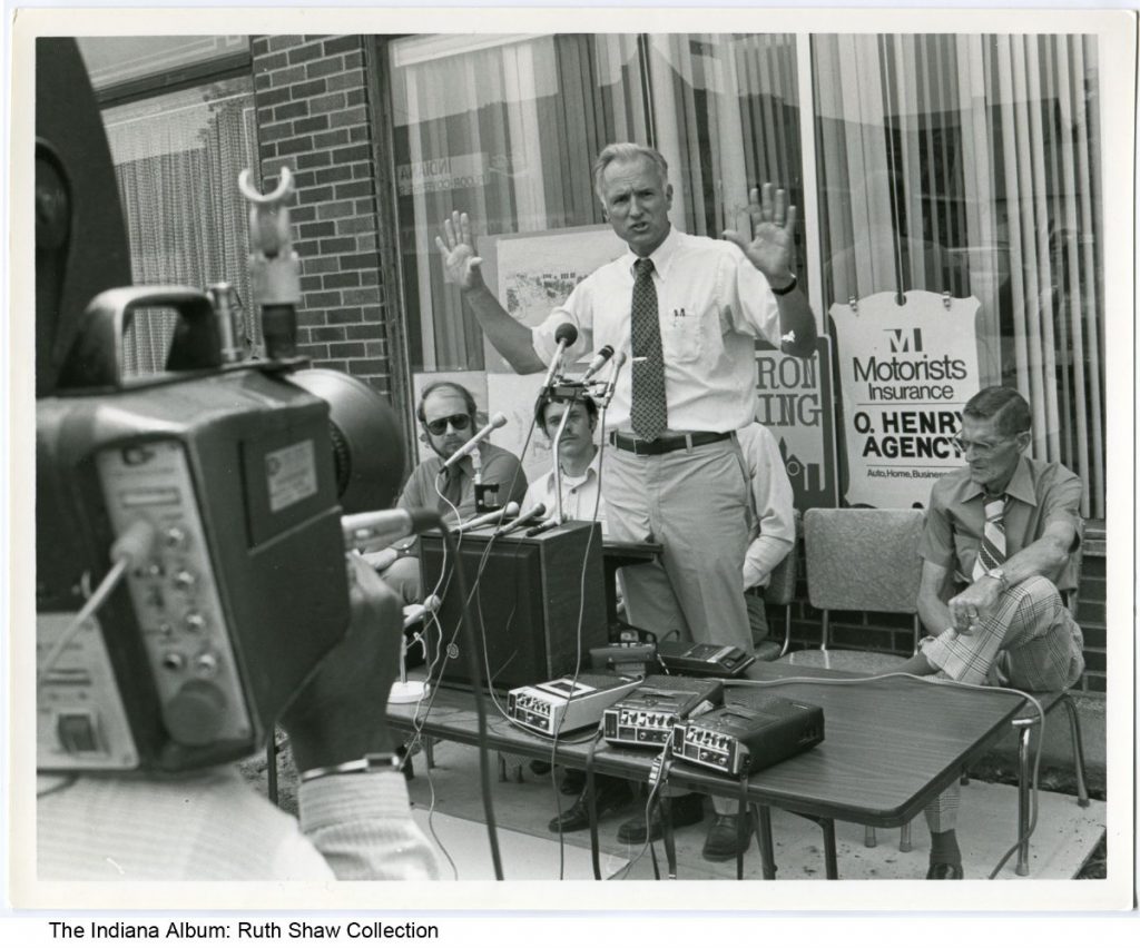 Mayor Hudnut stands in front of a camera and several recording devices.