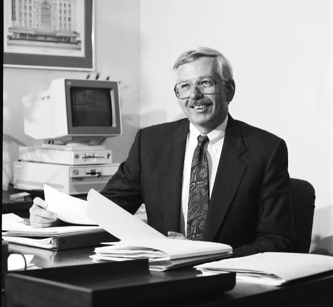Dr. William M. Plater sits at a desk and holds up some paper.
