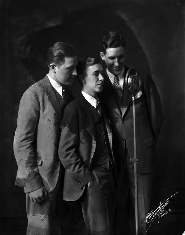 Three men stand in front of a standing microphone. 