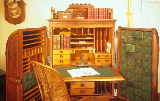 A large desk with two doors that are open. The desk has a fold down writing surface and a series of drawers and cubbies. 