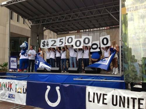 A group of people stand on a stage and hold up large numbers that together read "$42500000."