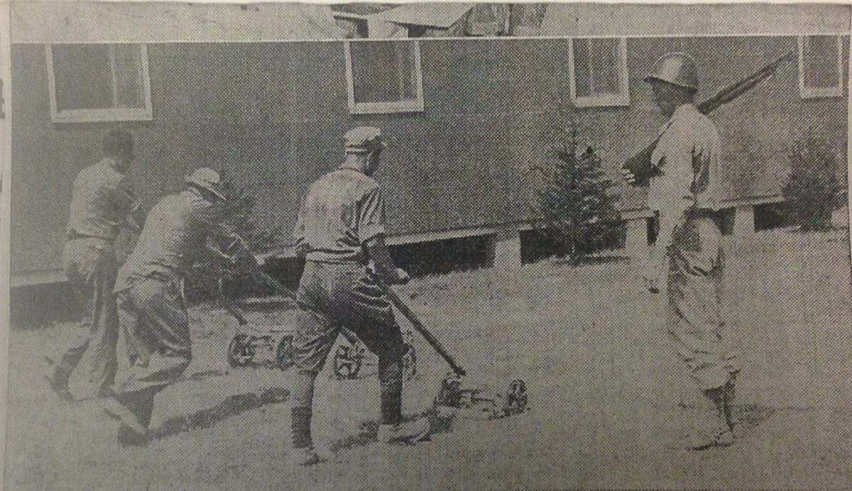 Three soldiers are mowing the lawn while another soldier watches.