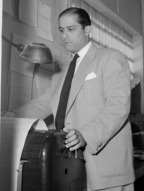 A man stands in front of a piece of equipment that prints news events. 