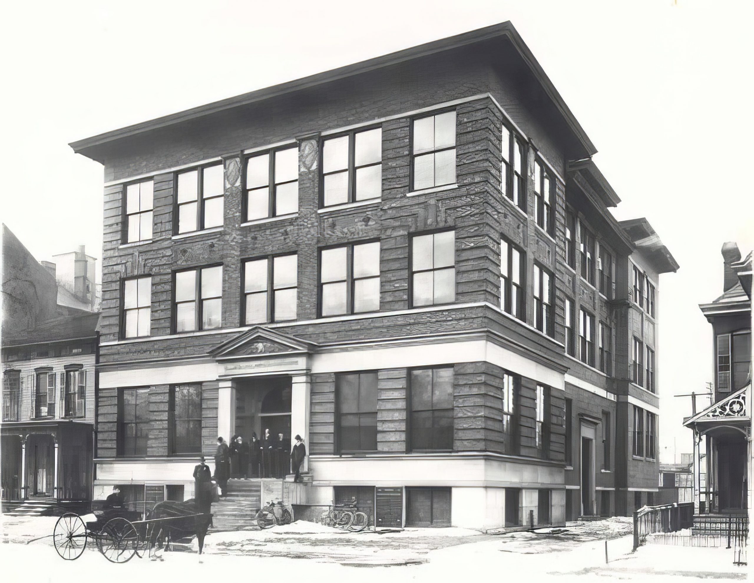A group of men stand outside a multi-story brick building. 