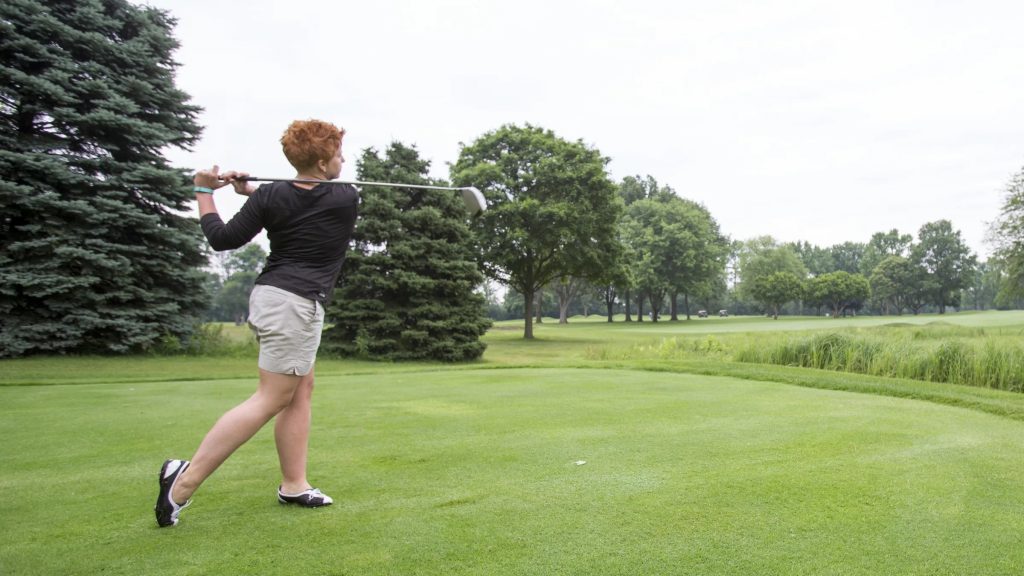 A woman tees off at a golf cource. 