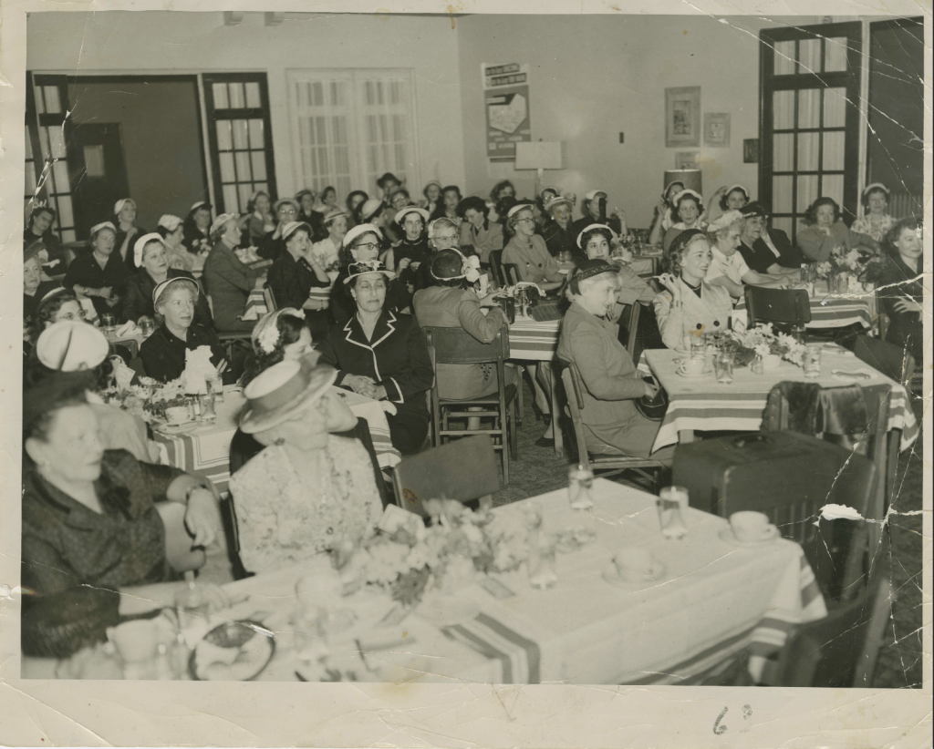 A large group of women sit at tables in a large room.