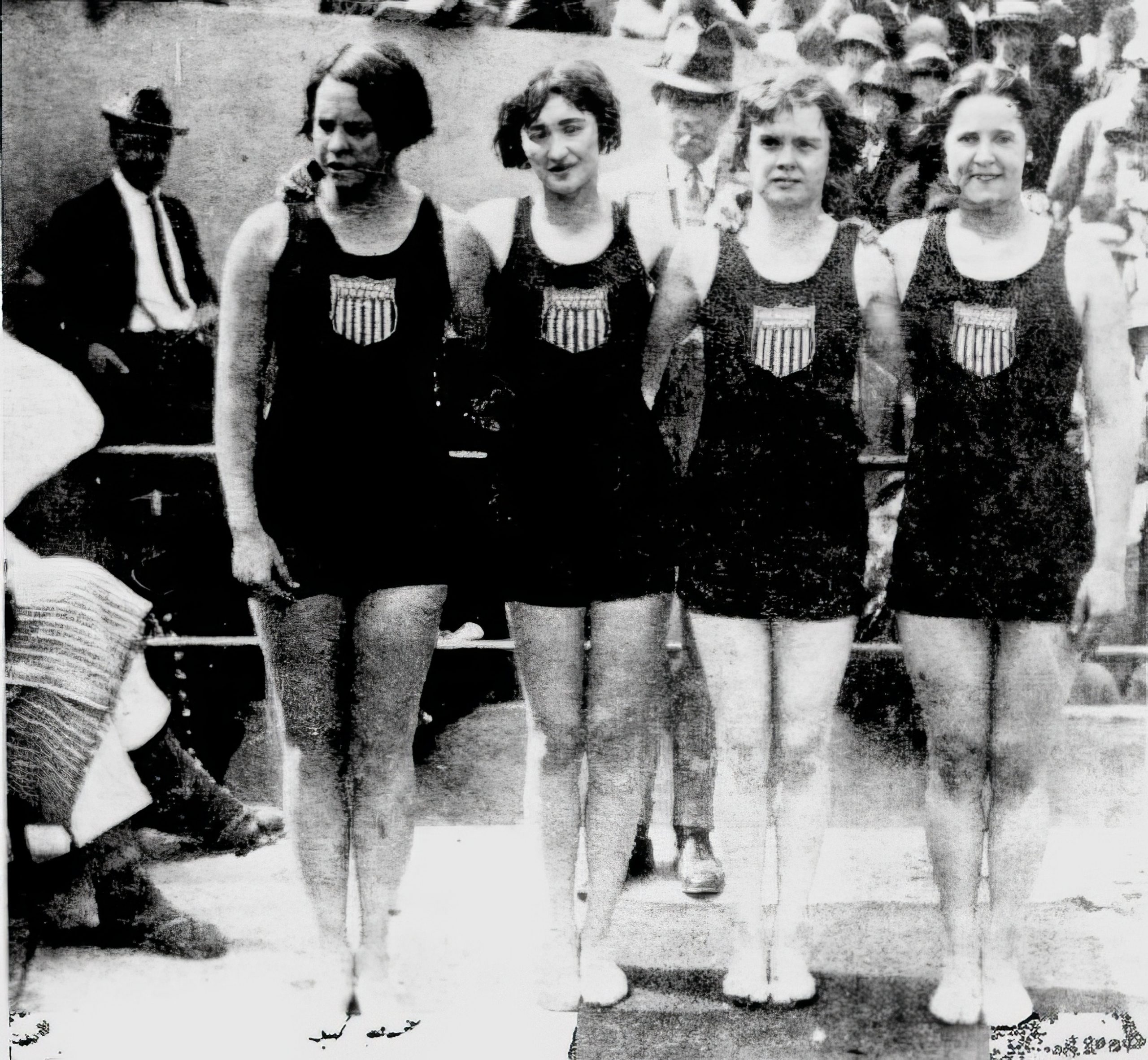Four young women stand together. They are all in swimsuits.