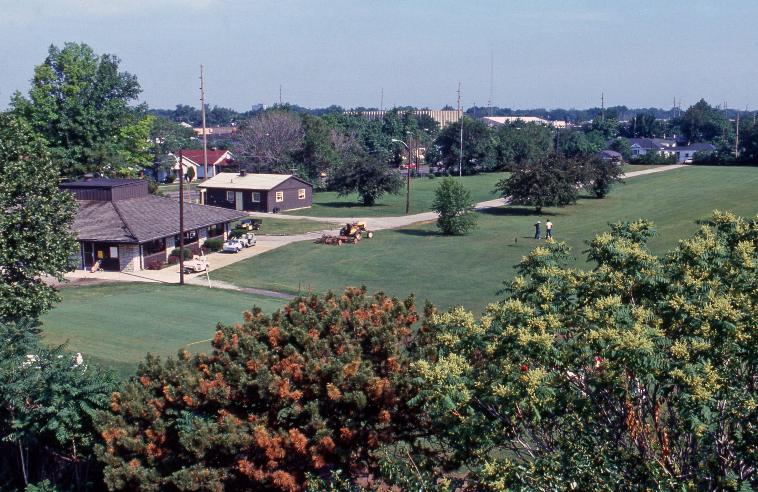 Aerial view of a golf course with a building in the background and trees in the foreground. 