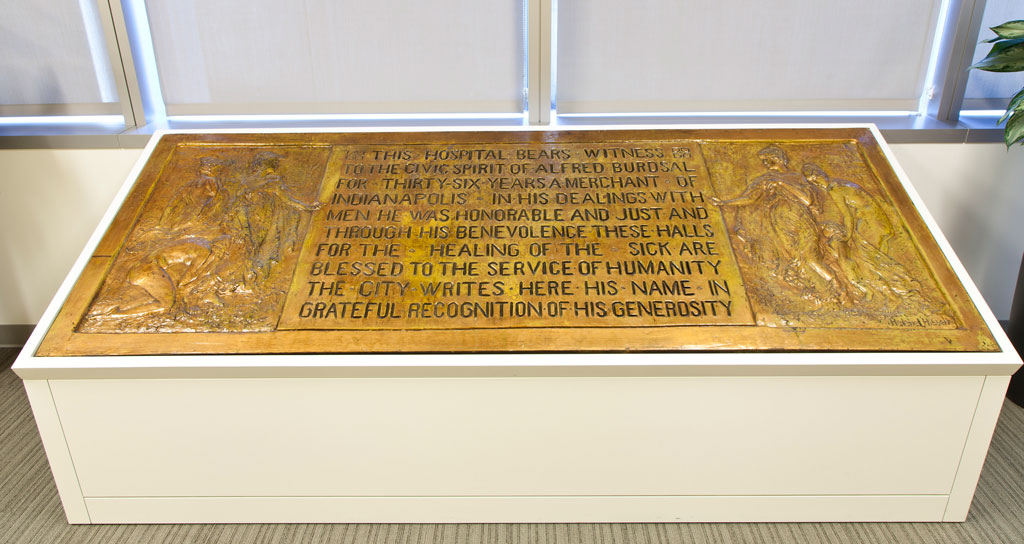 A large plaque rests on a display case. The plaque features text carved into the middle with two reliefs of people on either side. 