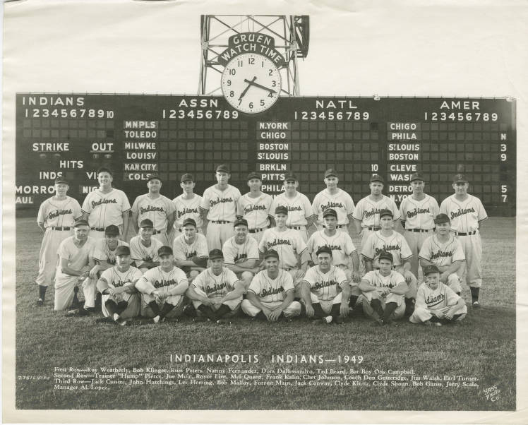 A baseball team is lined up in three rows in a baseball field. The scoreboard is in the background, and a list of the men's names at the bottom of the photograph.