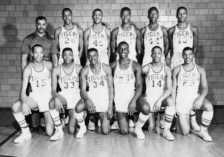 Two rows of young men in basketball uniforms pose with their coach.