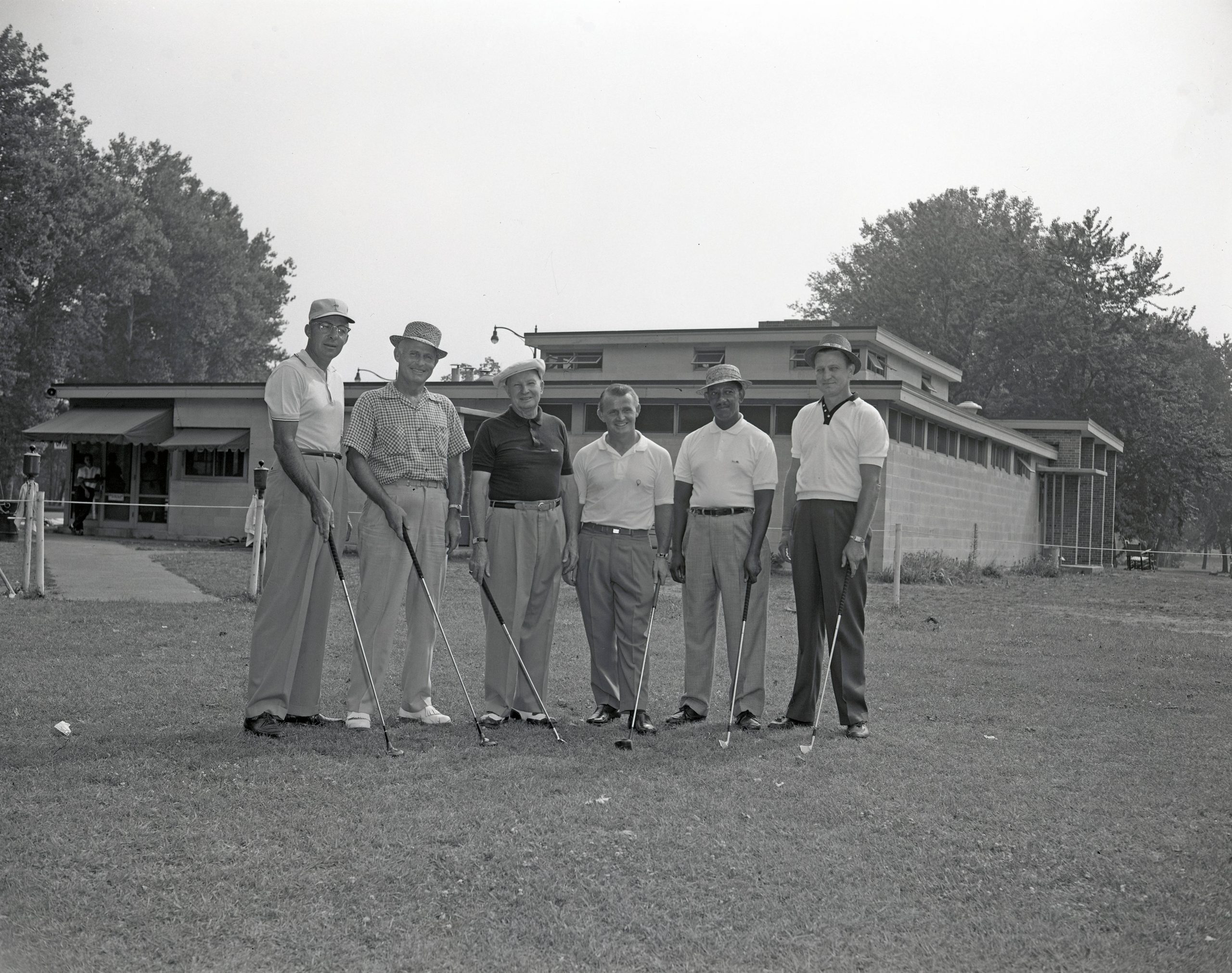 Six men stand with golf clubs on a golf course. 