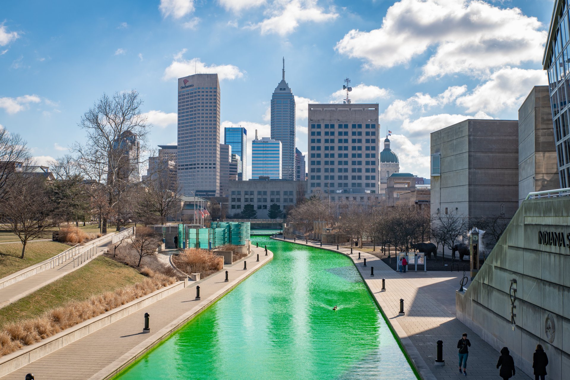 A view of the Canal Walk looking towards the downtown skyline. The water of the canal is bright green.