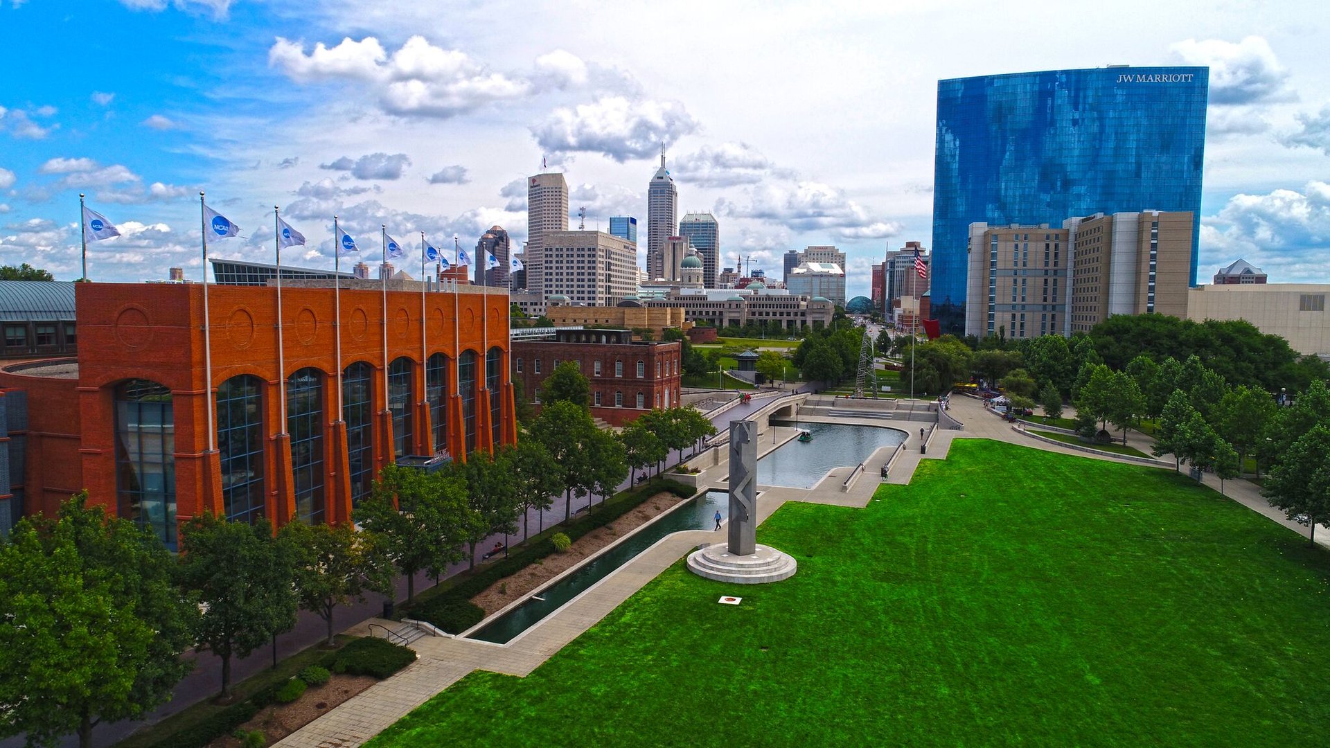 A view of the Canal corridor showing the NCAA headquarters building to the left of the canal and a green space to the right. The city skyline is in the background.