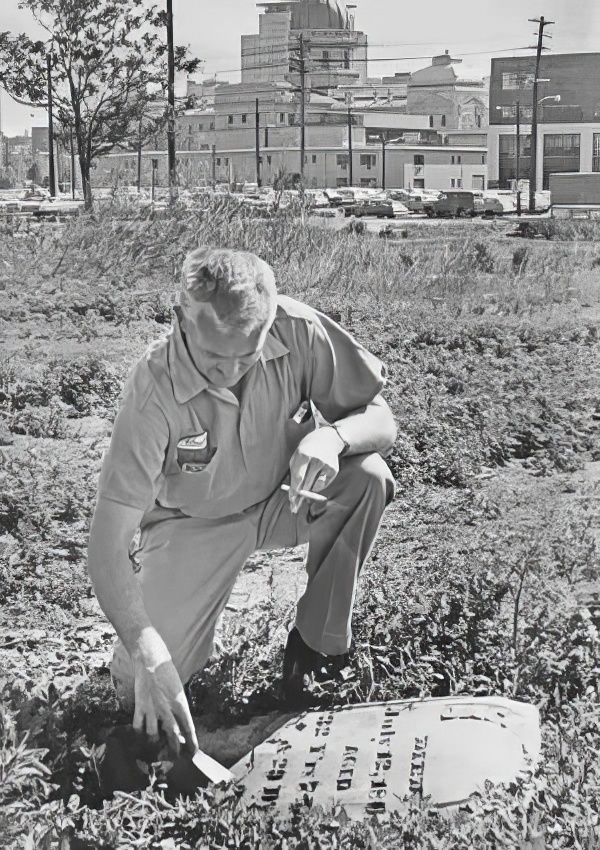 A man kneels down to inspect a fallen headstone. 