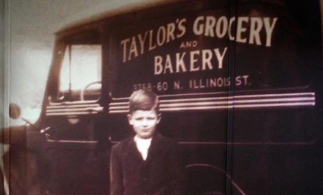 A young boy stands in front of a delivery truck. The truck reads "Taylors Grocery and Bakery."