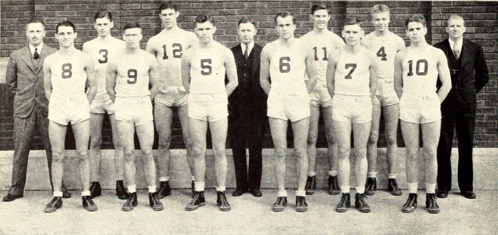 Basketball players in their uniforms and their coaches stand in a row. 