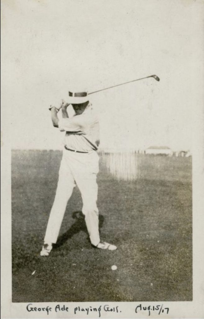 George Ade dressed in golf clothing is in mid-swing with a golf club. 