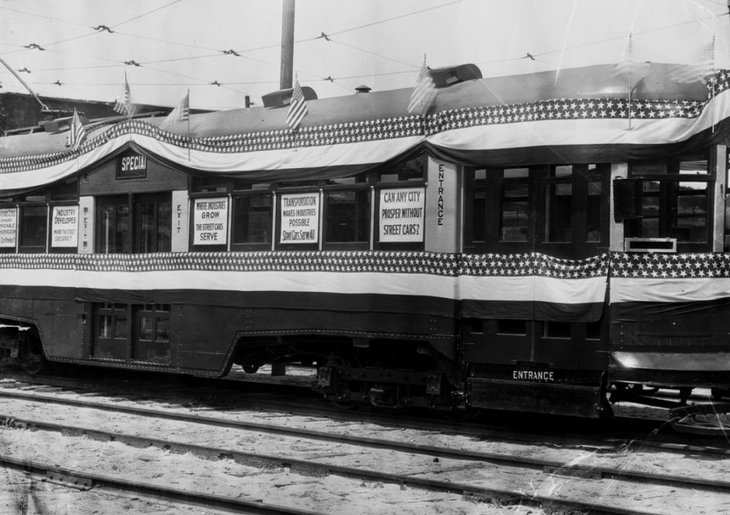 A parked street car with several sayings in the windows including "Can any city proper without street cars?"; "Transportation makes industries possible Street Cars Serve All"; and "Where industries grow The Street Cars serve."