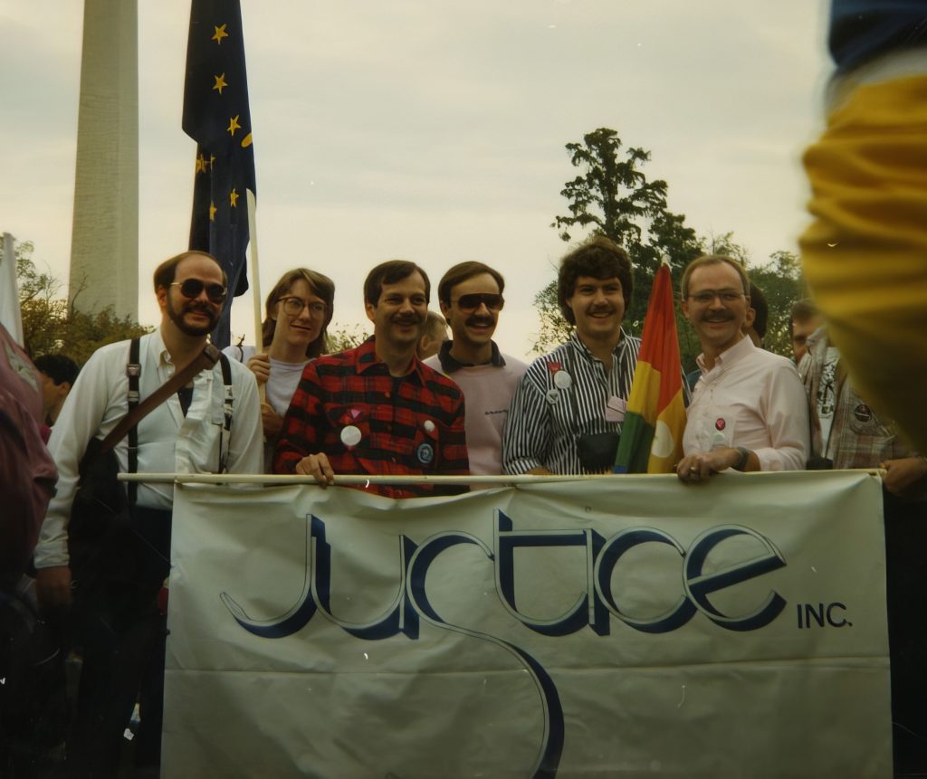 Several men and women hold a banner that says "Justice Inc."