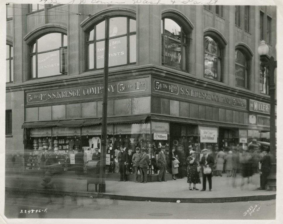 View of the S.S. Kresge Company store located on the southwest corner of Washington and Pennsylvania Streets. The store's windows are filled with merchandise on display. A crowd of people are on the sidewalk in front of the store. There is a mailbox at the corner.