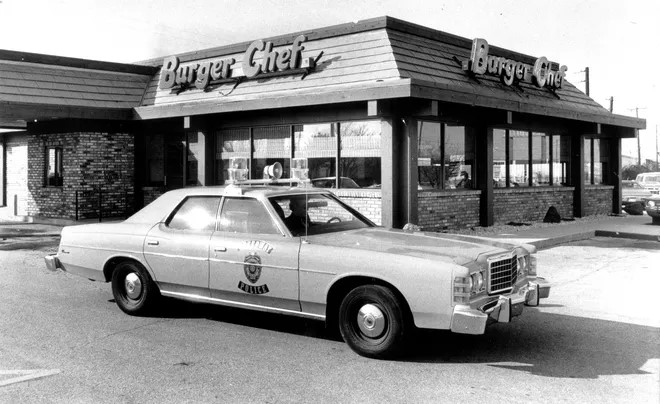 A police car is parked outside of a fast food restaurant. 