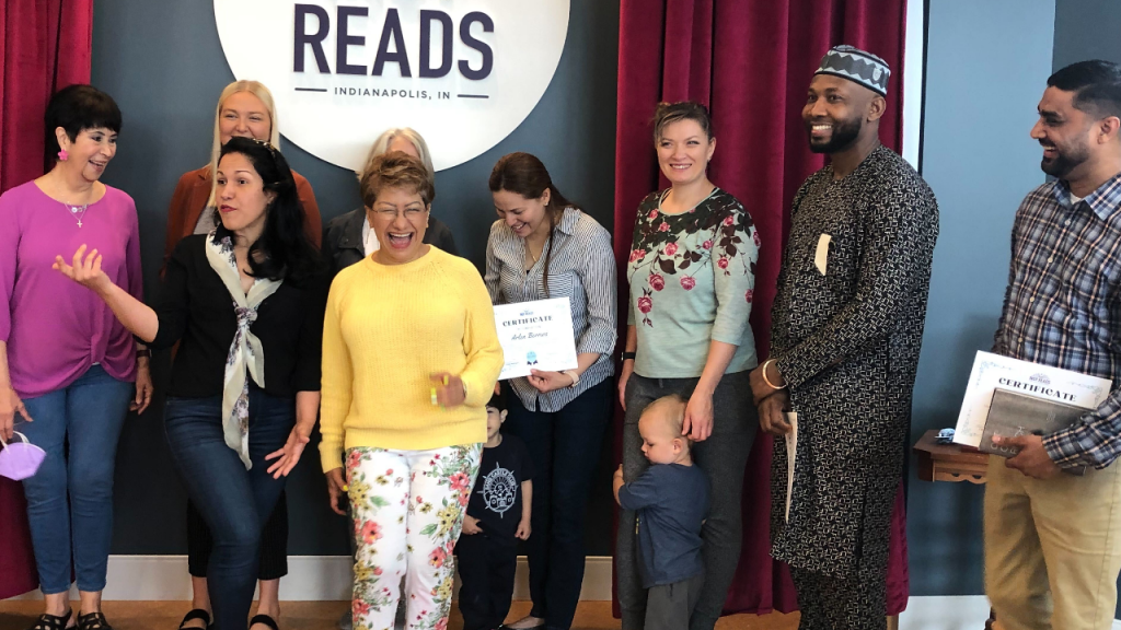 A group of adults stand together. A couple of the adults are holding up certificates. 