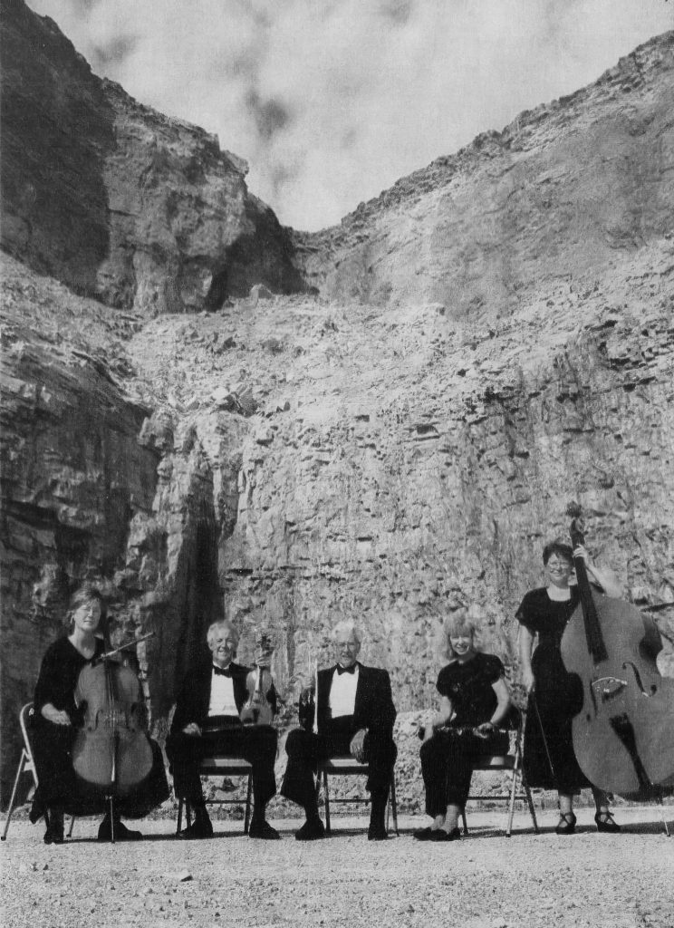 Five people are in a rock quarry, posing with their instruments. 