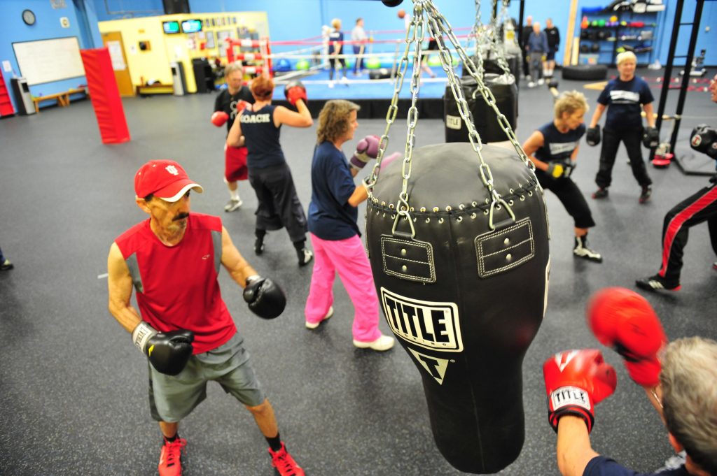 Several men and women stand in front of punching bags. 