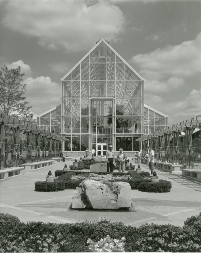 People walk around a pathway with the conservatory and its tropical plants in the background.