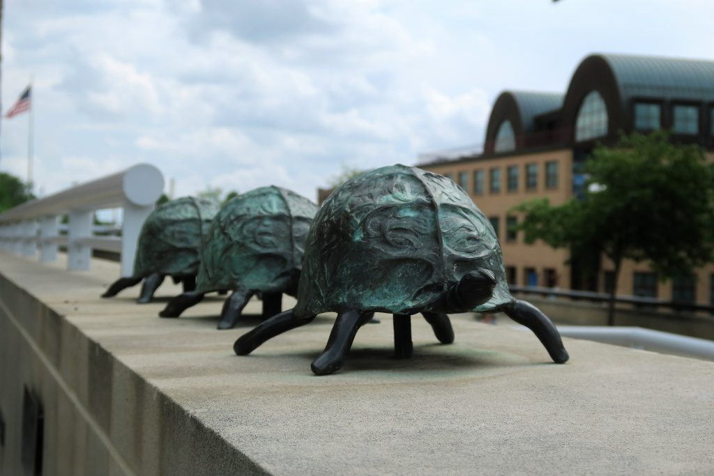 Three bronze turtles are in a line on top of a wall. 