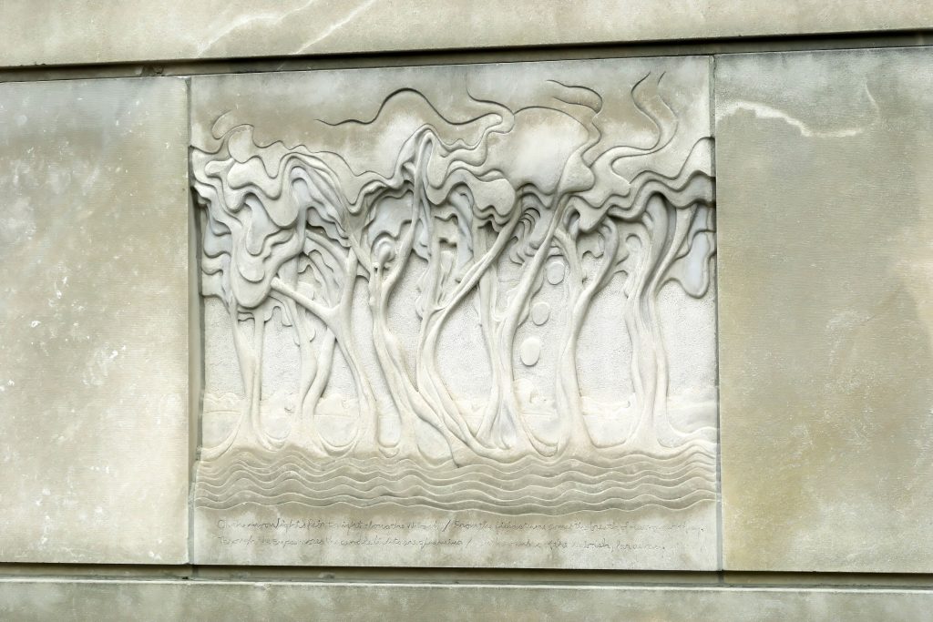 A sculpture on a wall that features abstract trees with human-like shapes as the trunks. 