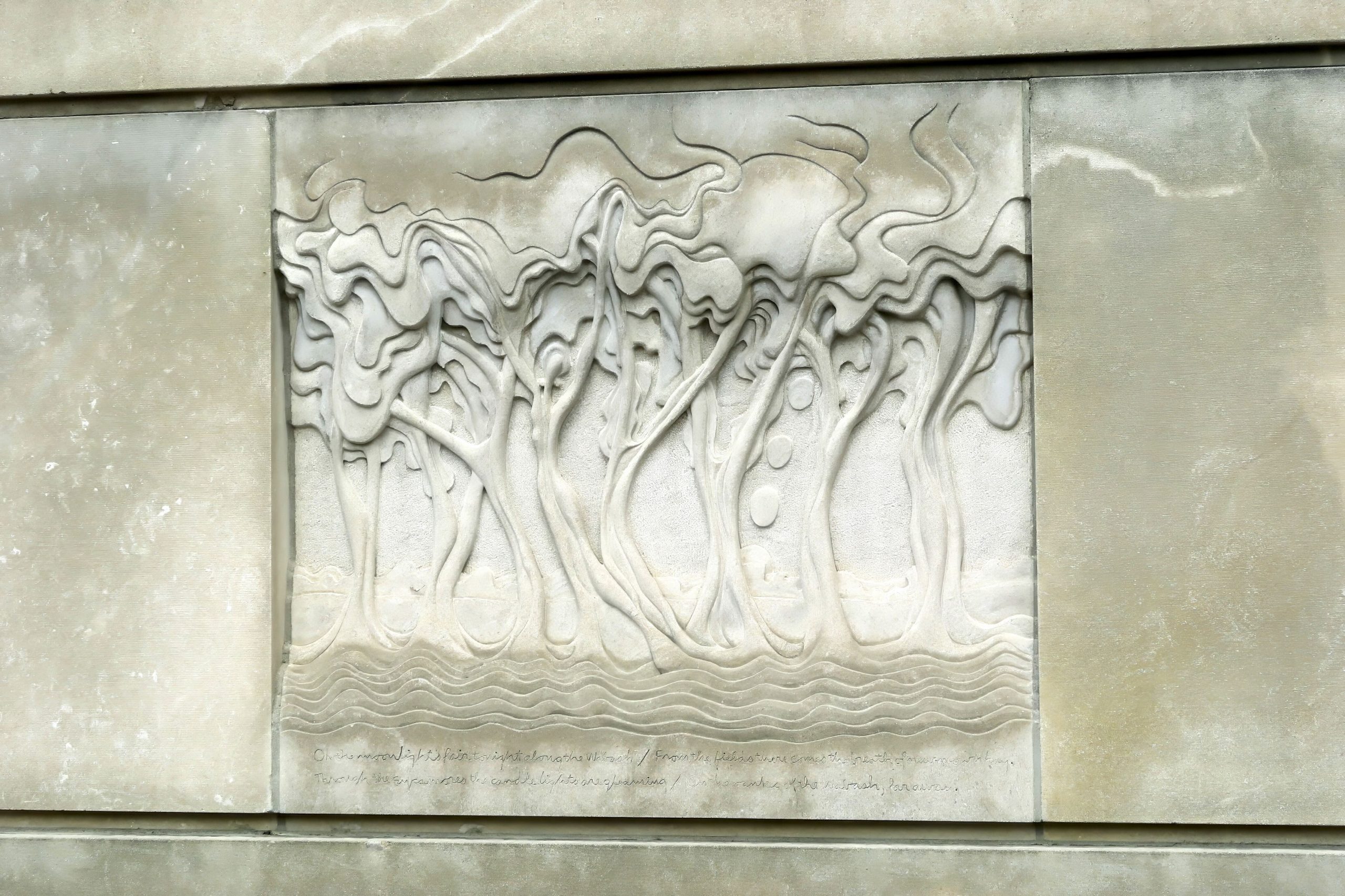 A sculpture on a wall that features abstract trees with human-like shapes as the trunks.