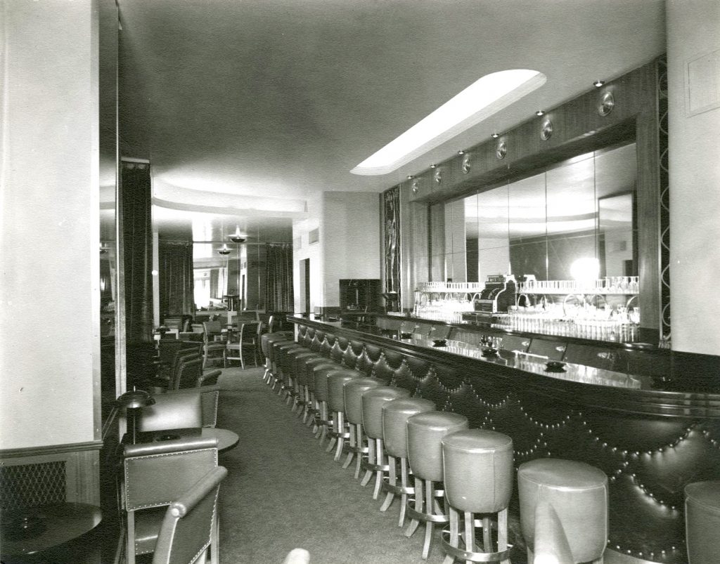 A long bar with a mirror behind it. Round stools line the front of the bar. 