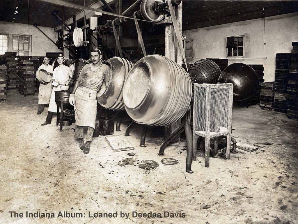 Three men in aprons stand in front of large industrial mixing vats. 