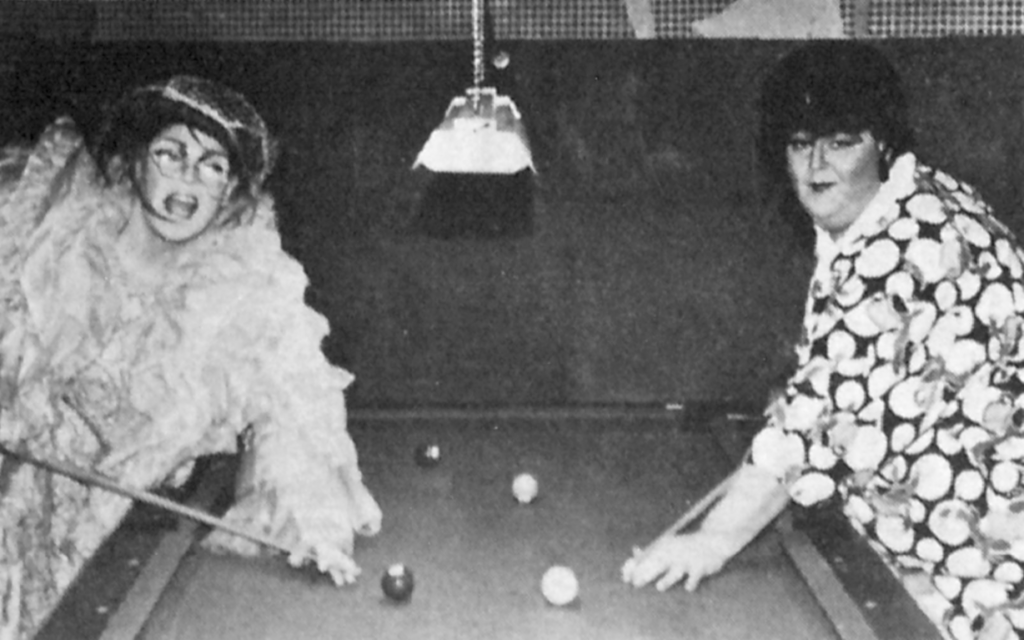 Two people in drag play pool. 