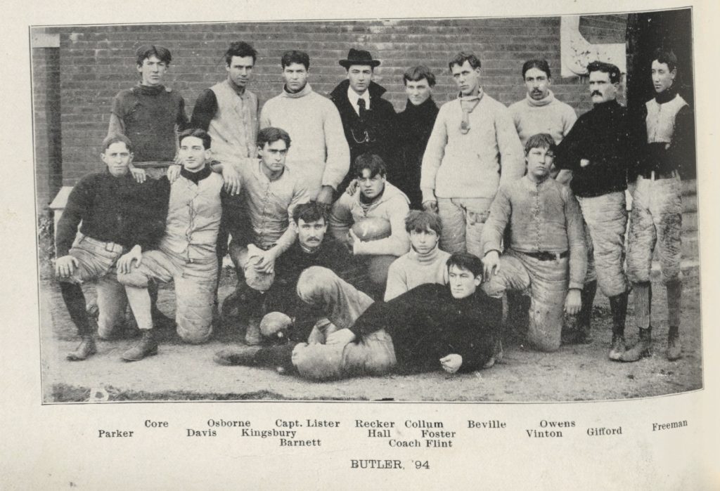 Seventeen young men pose together. The man in the middle is holding a football. 