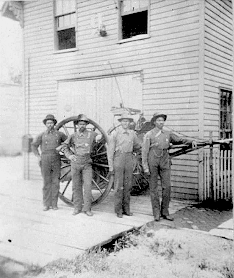 Four Black men stand in front of a large cart.