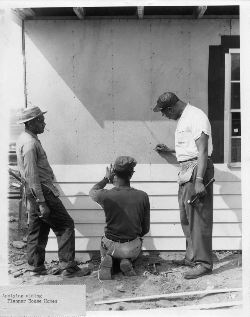 Three men work on applying plank siding to the front of a single story home.