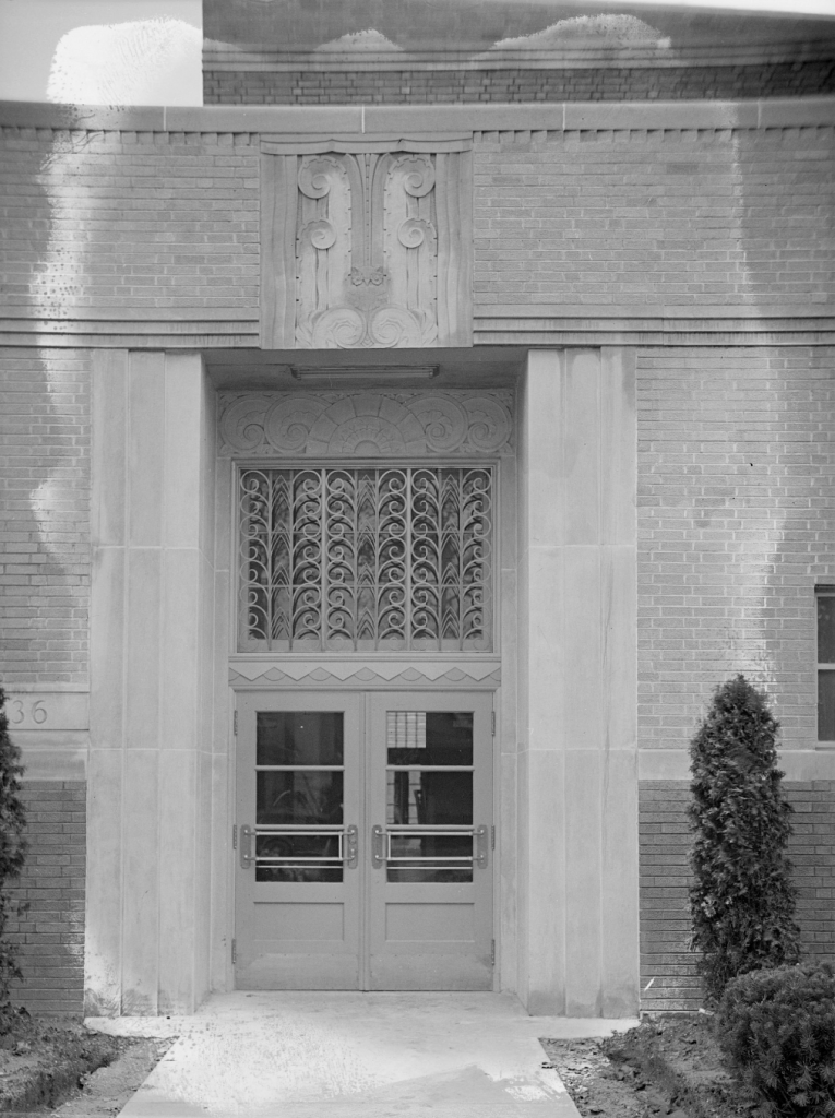 This exterior photo of the James E. Roberts School shows one of the entryways into the school. The limestone features decorative carving, while the window above the doors features decorative metalwork.