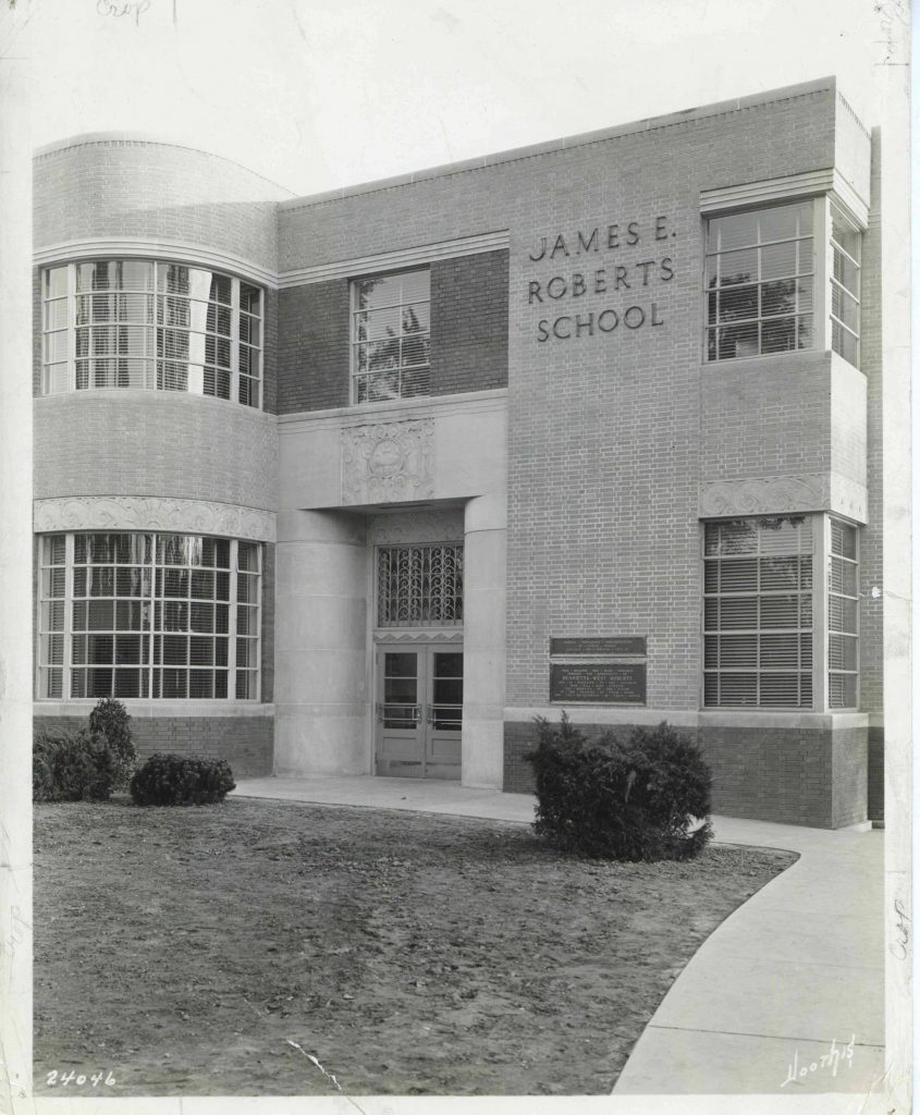 Close up view of the front of a multi-story brick school building. The style is modern with squared windows and a curved wall protruding from the far side of the double entrance doors.