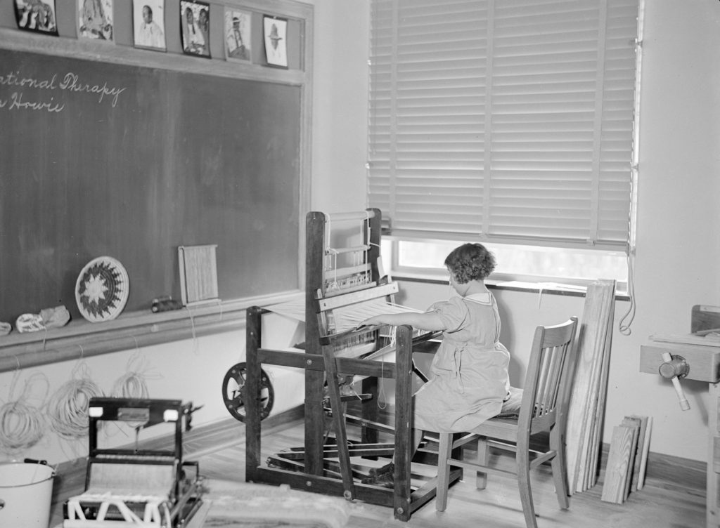 A young girl weaves material at a loom in a classroom at James E. Roberts School.