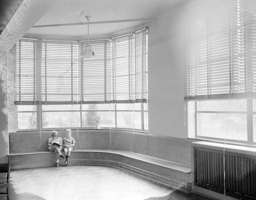 This interior photo of the James E. Roberts School shows two children at a rounded window seat. They are reading a book together.