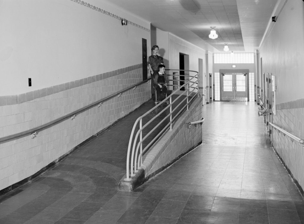 A woman pushes a boy in a wheelchair down the ramp at the James E. Roberts School.