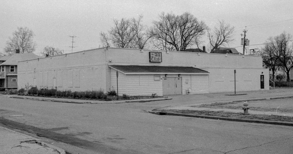Exterior view showing the front of a building. The sign centered over the front entrance reads "The 21 Club".
