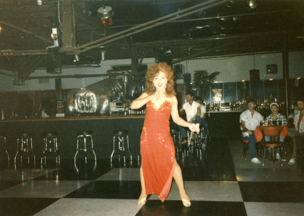 A drag performer stands in the middle of a dance floor.