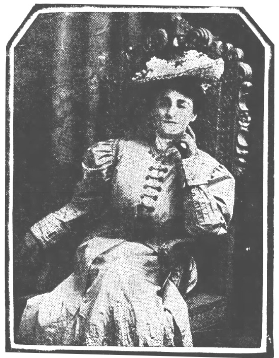 Portrait of a woman sitting in a chair and holding her hand up to her face.