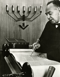 A man uses a yad and recites from a torah.